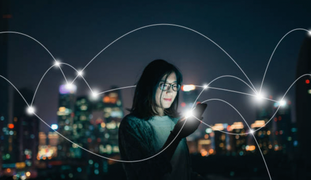 A woman in glasses looks at her phone at night with city lights and glowing lines connecting points in the background